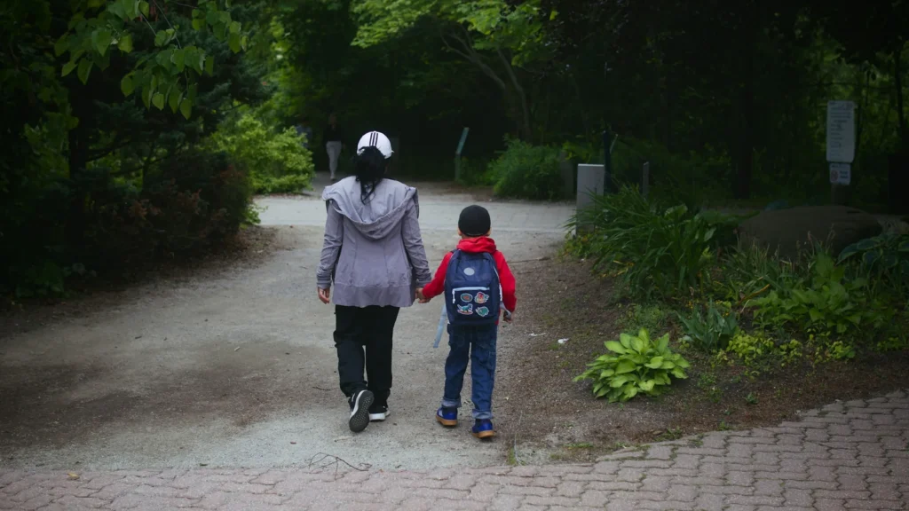 緑の小道を手をつないで歩く親子の後ろ姿